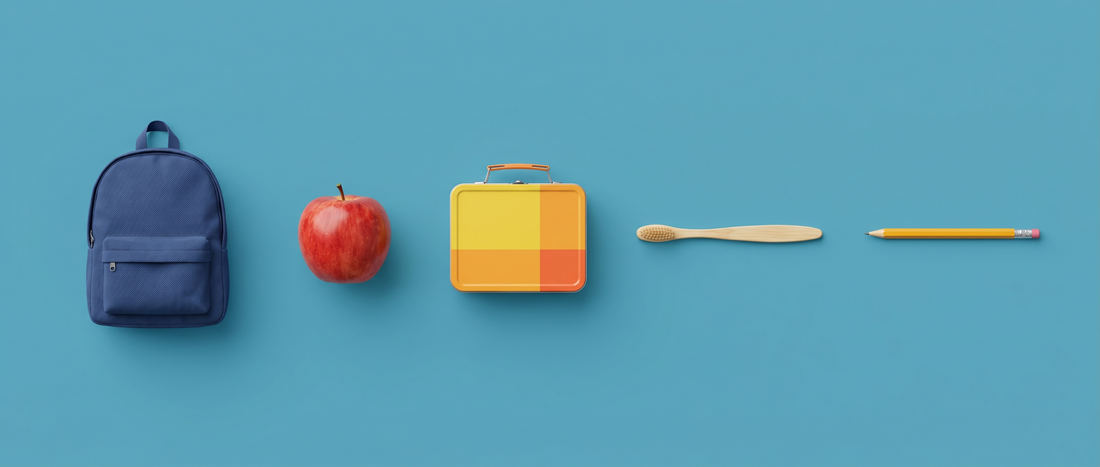 Navy school backpack, red apple, lunchbox, bamboo toothbrush and pencil on a mid-blue background
