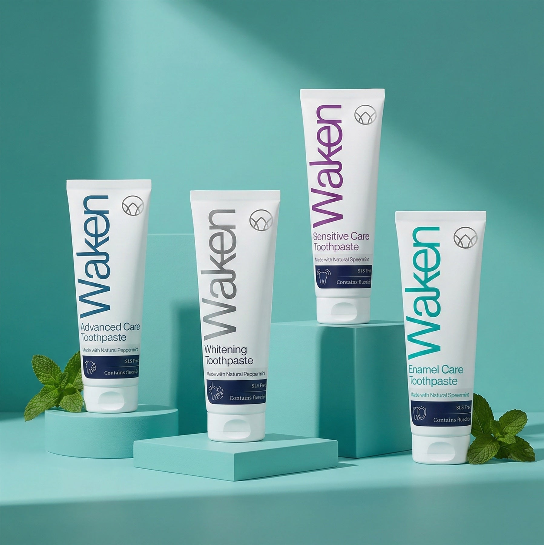 The four Waken toothpastes on teal blocks with mint leaves